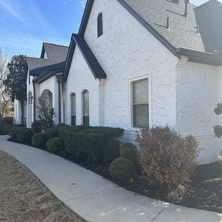 A white textured house exterior with arched windows and a black roof.