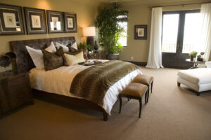 Bedroom with earthy colors, including tan walls with reddish glow in artificial lighting and dark brown baseboards and patio door framewn baseboards 