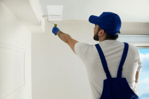 A handyman painting a ceiling in white paint.