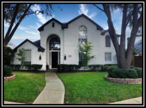 Picture of the front of a large white house with an arched entryway and a tree in the front yard.